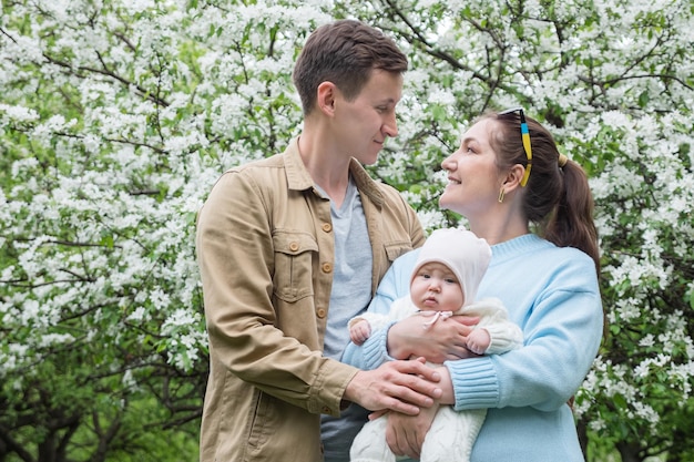 Une famille avec une fille nouveau-née se tient dans le jardin des pommiers en fleurs