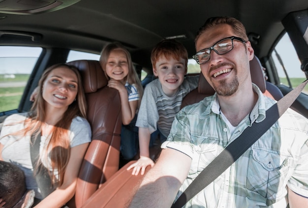 La famille gaie avec deux enfants va à la voiture