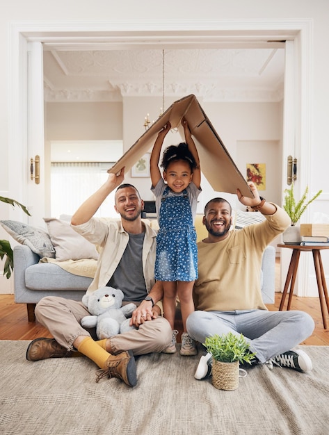 Photo une famille gay heureuse et un enfant avec une maison en carton ou un toit avec de l'amour, des soins et de la sécurité dans un salon. hommes lgbtq, adoption et parents avec une fille adoptive.