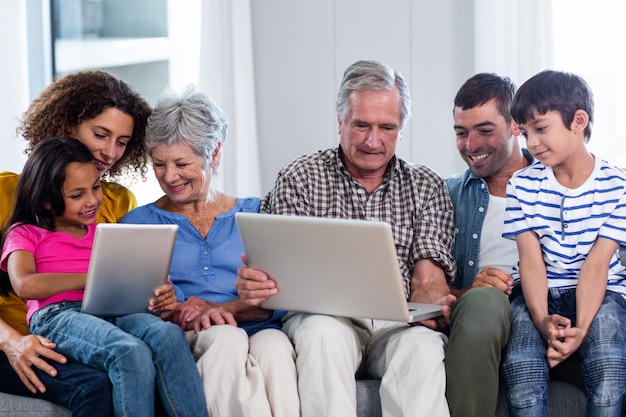 Famille heureuse à l'aide d'un ordinateur portable et d'une tablette numérique dans le salon