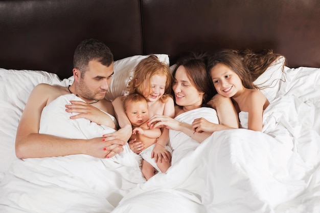 Famille heureuse allongée sous une couverture au lit à la maison