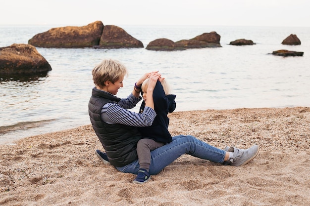 Famille heureuse assis sur la plage de la mer à l'automne Femme avec fils s'amuser en vacances près de l'océan Voyage amour vacances concept lifestyle