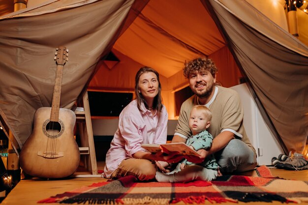 Famille heureuse avec un beau bébé jouant et passant du temps ensemble dans le glamping le soir d'été Tente de camping de luxe pour les loisirs de plein air et les loisirs Concept de style de vie