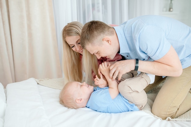 Famille heureuse avec un bébé mignon. Maman, papa, fils jouent sur le lit dans une pièce lumineuse et confortable à la maison.