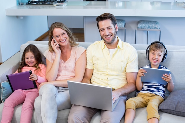 Famille heureuse sur le canapé ensemble à l&#39;aide d&#39;appareils