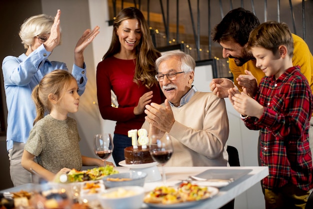 Famille heureuse célébrant l'anniversaire de grand-père avec un gâteau et des bougies à la maison