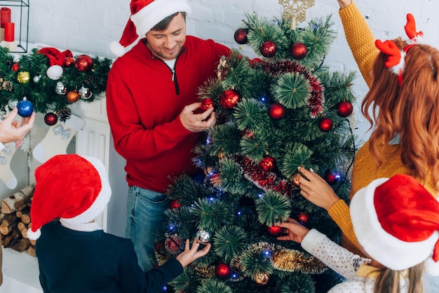 Famille heureuse en chapeaux de père noël décorant le sapin de noël ensemble à la maison