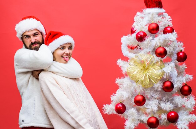 Famille heureuse en chapeaux de père Noël s'amusant près de l'arbre de Noël couple heureux s'amuser tout en