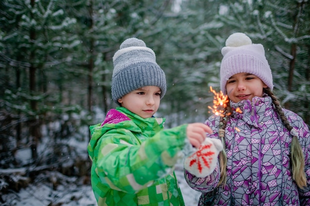 Famille heureuse avec des cierges magiques brûlants pendant la marche dans la forêt le jour de neige célébration de noël