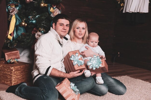 Famille heureuse avec des coffrets cadeaux assis près de l'arbre de Noël la veille de Noël. concept de vacances