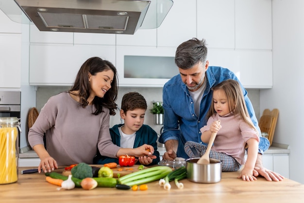 Une famille heureuse cuisinant ensemble dans la cuisine Mère Fils et fille avec le père cuisinant Fils et mère coupant des légumes verts Récréation à la maison et préparation de la nourriture le week-end