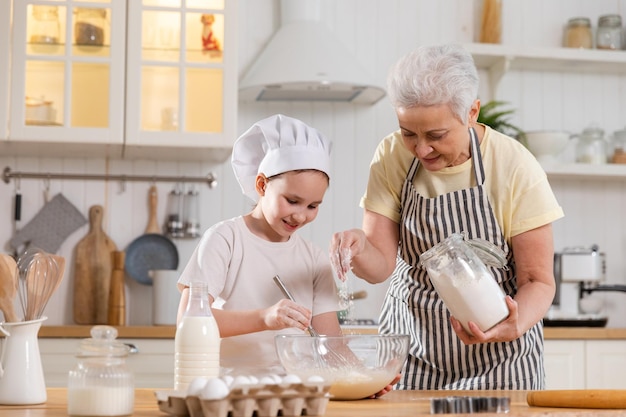 Famille heureuse dans la cuisine Grand-mère et petite-fille enfant cuisinent dans la cuisine ensemble Grand-mère enseignant enfant fille pétrir la pâte cuire des biscuits Travail d'équipe domestique aidant le concept des générations familiales