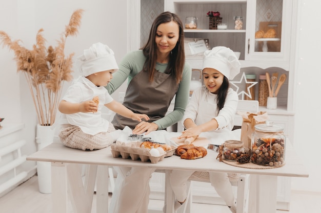 Famille heureuse dans la cuisine. maman et enfants en costumes de cuisinier dans la cuisine. maman et enfants préparent la pâte, font des biscuits