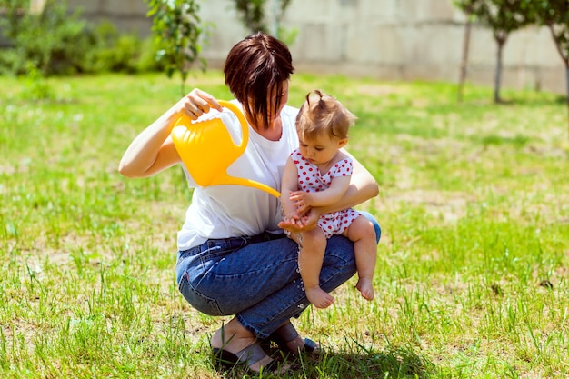 Famille heureuse dans le jardin. l'eau d'un arrosoir est versée dans les mains de l'enfant. mère lave ses mains à un enfant dans le jardin d'un arrosoir jaune.