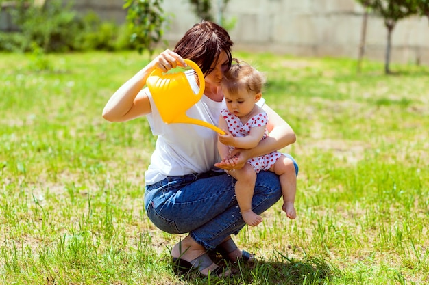 Famille heureuse dans le jardin. l'eau d'un arrosoir est versée dans les mains de l'enfant. mère lave ses mains à un enfant dans le jardin d'un arrosoir jaune.