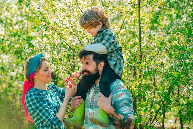 Famille heureuse dans le jardin Mode de vie et vie de famille Petit garçon avec père et mère dans un verger au printemps Vie à la campagne Couple avec fils jardinant dans le jardin de la cour