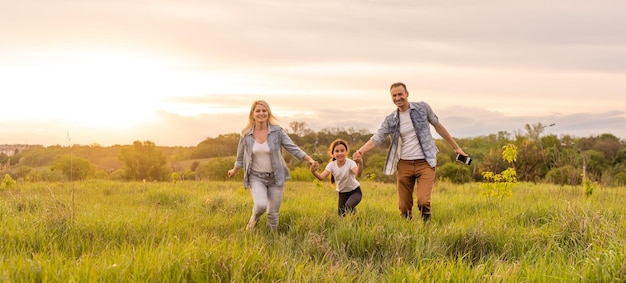 Famille heureuse dans la lumière du soir du parc. Les lumières d'un soleil. Maman, papa et bébé se promènent au coucher du soleil. Le concept d'une famille heureuse.