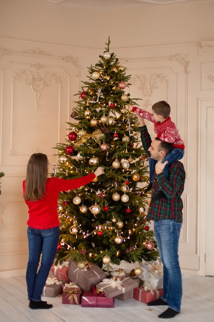 Une famille heureuse décore l'arbre de Noël à l'intérieur ensemble. Famille aimante. Joyeux Noël et bonnes vacances