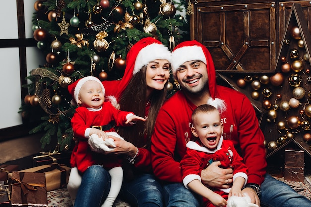 Famille heureuse avec deux enfants adorables s'amusant à l'arbre de Noël