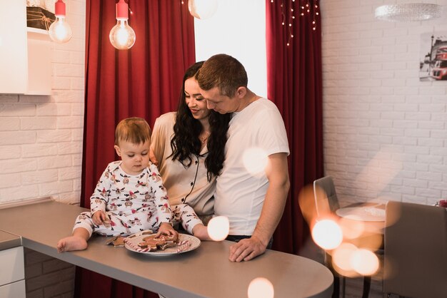 Famille heureuse avec enfant célébrant le Nouvel An et Noël à l'arbre de Noël décoré et aux guirlandes