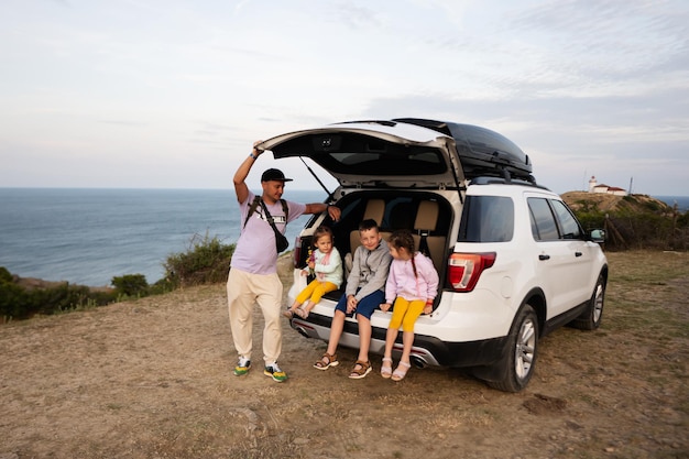 Une famille heureuse avec des enfants assis dans le coffre de la voiture et regardant la mer.