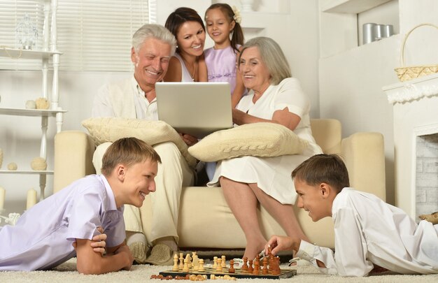 Famille heureuse avec enfants sur canapé dans le salon avec ordinateur portable, garçons jouant aux échecs