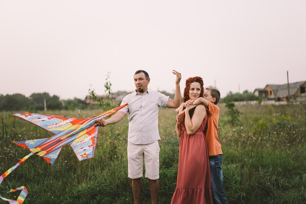 Une famille heureuse et des enfants courent sur un pré avec un cerf-volant en été sur la nature Famille jouant avec un cerf-volant tout en courant le long d'un champ d'été rural Journée familiale