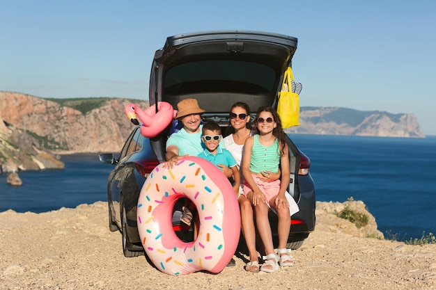 Une famille heureuse est assise dans le coffre d'une voiture avec vue sur la mer