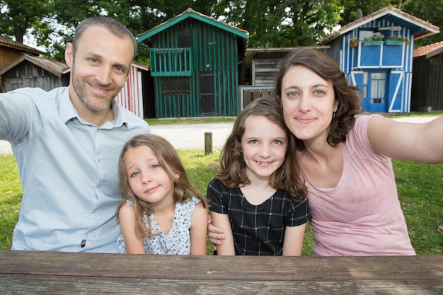 Famille heureuse à l'extérieur avec cabane en bois à l'arrière-plan faire selfie photo mère père et fille