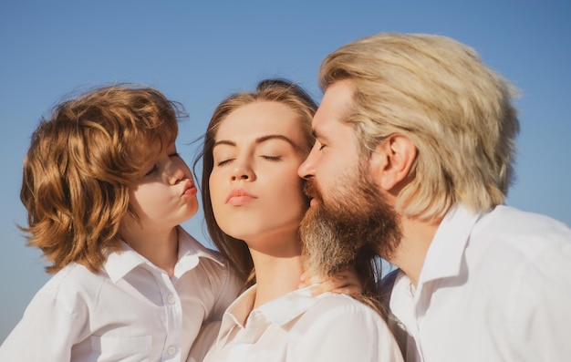 Famille heureuse à l'extérieur Père et fils embrassent et embrassent la mère Jeune famille souriante avec enfant s'amusant ensemble Les enfants aiment et étreignent maman Visage souriant Fête des mères Parents et enfants