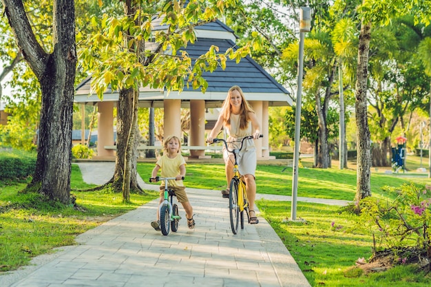 Une famille heureuse fait du vélo à l'extérieur et une maman souriante sur un vélo et son fils sur un vélo d'équilibre