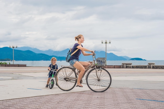 Une famille heureuse fait du vélo à l'extérieur et sourit. Maman sur un vélo et son fils sur une draisienne