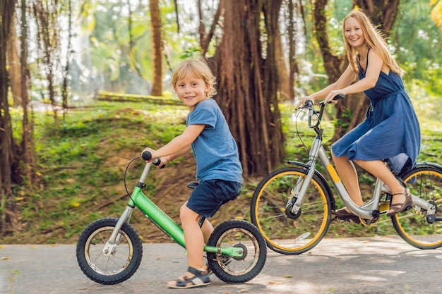 Une famille heureuse fait du vélo à l'extérieur et sourit. Maman sur un vélo et son fils sur une draisienne