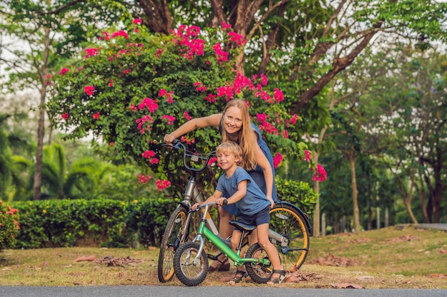 Une famille heureuse fait du vélo à l'extérieur et sourit. Maman sur un vélo et son fils sur une draisienne