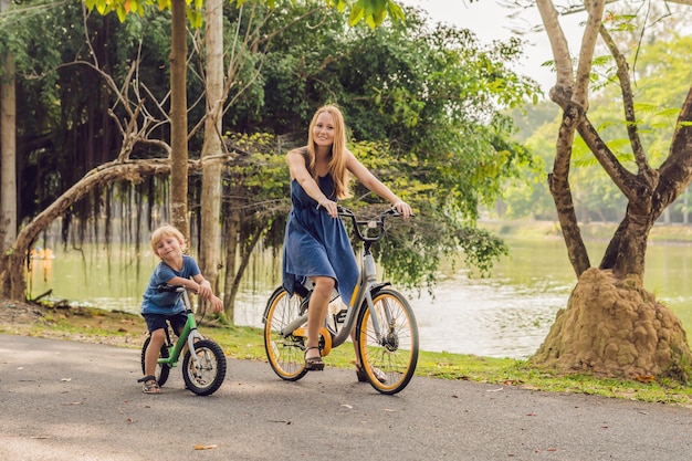 Une famille heureuse fait du vélo à l'extérieur et sourit. Maman sur un vélo et son fils sur une draisienne