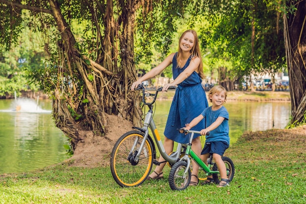 Une famille heureuse fait du vélo à l'extérieur et sourit. Maman sur un vélo et son fils sur une draisienne