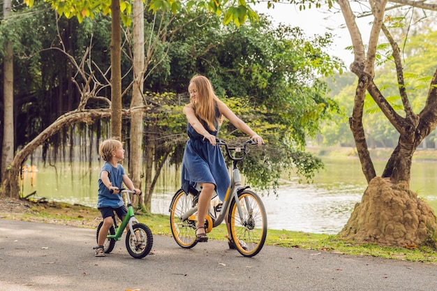 Une famille heureuse fait du vélo à l'extérieur et sourit. Maman sur un vélo et son fils sur une draisienne