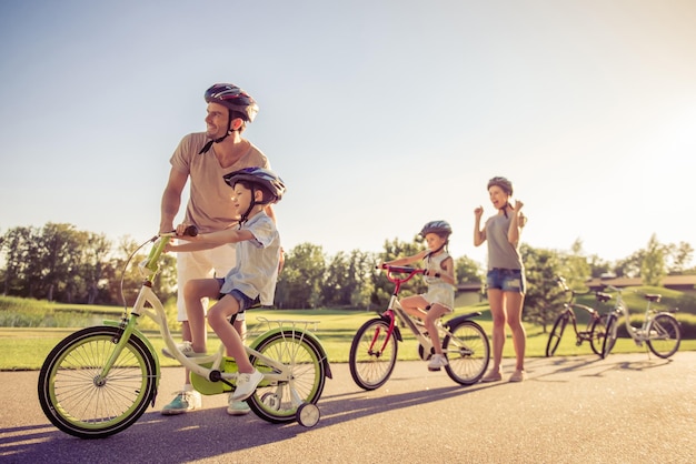 Une famille heureuse fait du vélo à l'extérieur et sourit Les parents enseignent à leurs enfants Maman tient les poings