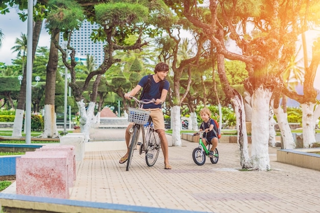 Une famille heureuse fait du vélo à l'extérieur et sourit. Père en vélo et fils en draisienne.