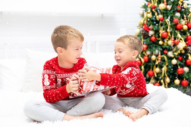 Famille heureuse un garçon et son frère regardent des cadeaux, les enfants sont à la maison pour les vacances de Noël. Les vacances du nouvel an. Enfants dans une salle décorée de façon festive avec un sapin de Noël.