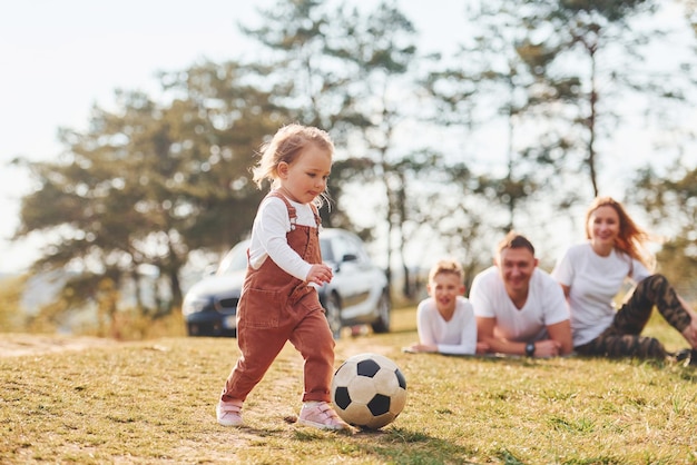 Famille heureuse jouant avec un ballon de soccer à l'extérieur près de la forêt avec sa fille et son fils