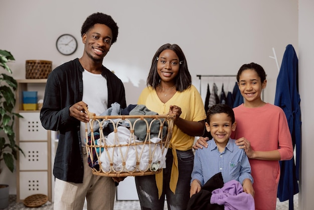 La famille heureuse et joyeuse fait les tâches ménagères ensemble dans la buanderie les parents tiennent le panier