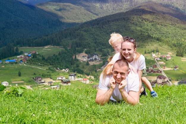 Famille heureuse. joyeux père, mère et deux fils sont allongés sur l'herbe verte dans le contexte de la forêt, des montagnes et du ciel avec des nuages.