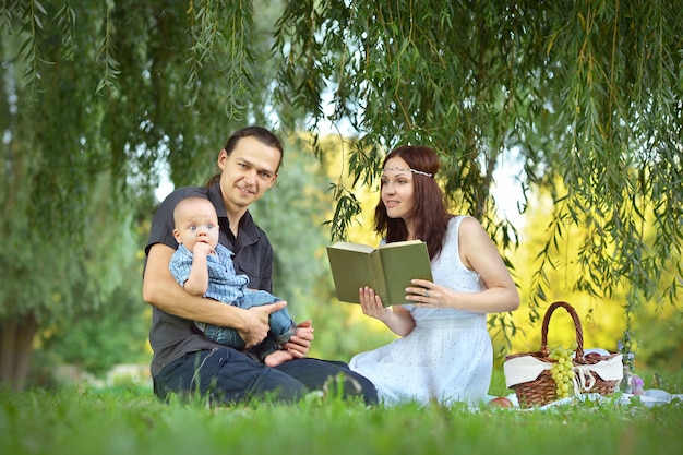 Famille heureuse lisant un livre au petit fils au pique-nique dans le parc