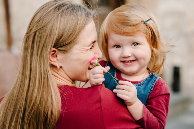 Famille heureuse : maman embrasse sa fille avec un bouquet de fleurs, profitant du temps ensemble, se tenir dans la rue de la ville du pays Europa.