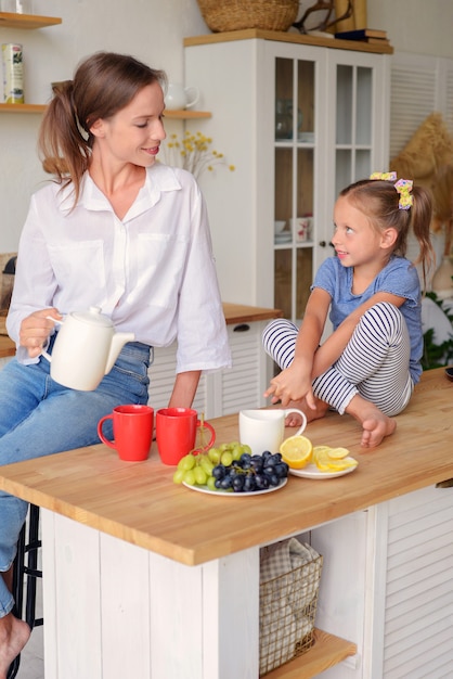 famille heureuse maman et fille boivent du thé dans la cuisine petit déjeuner familial