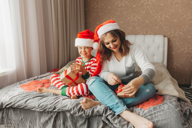 Famille heureuse, maman et fils, étreignant et offrant des cadeaux au lit le matin de Noël. Noël.