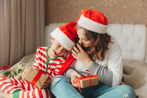 Famille heureuse, maman et fils, étreignant et offrant des cadeaux au lit le matin de Noël. Noël.