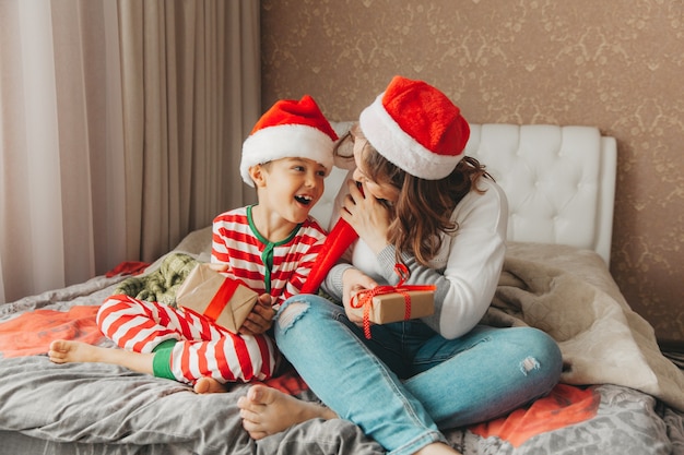 Famille heureuse, maman et fils, étreignant et offrant des cadeaux au lit le matin de Noël. Noël.