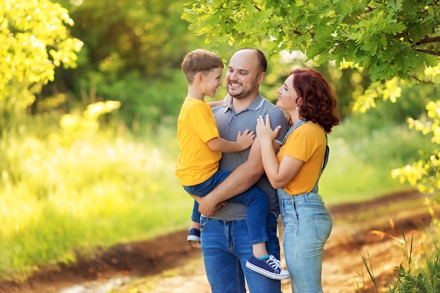 Famille heureuse, maman, papa, fils marchent, s'embrassent à l'extérieur en été.